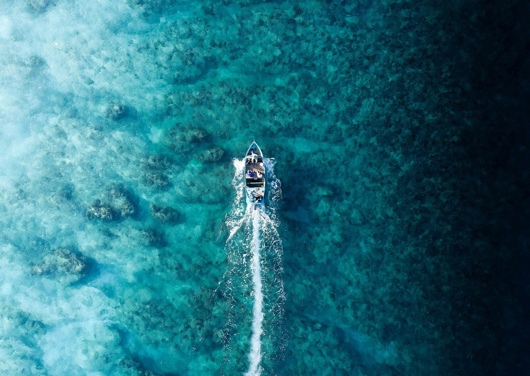 Aerial view of a small boat cutting a white wake across deep turquoise and blue water