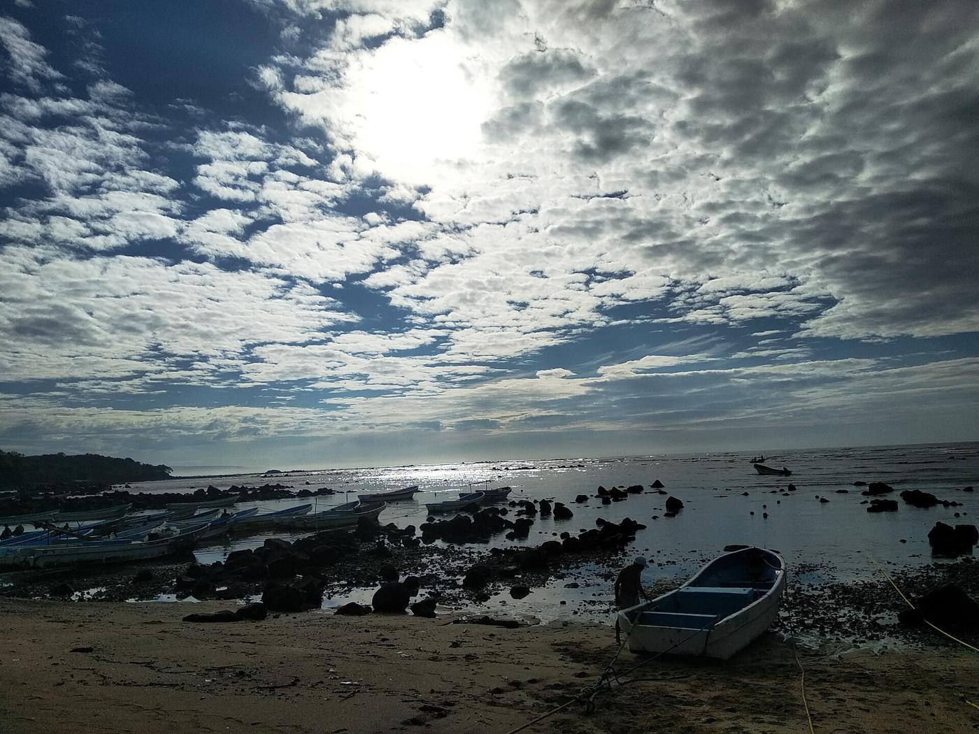 A small fishing boat pulled up on a rocky volcanic shore under a dramatic cloudy sky at Los Cóbanos