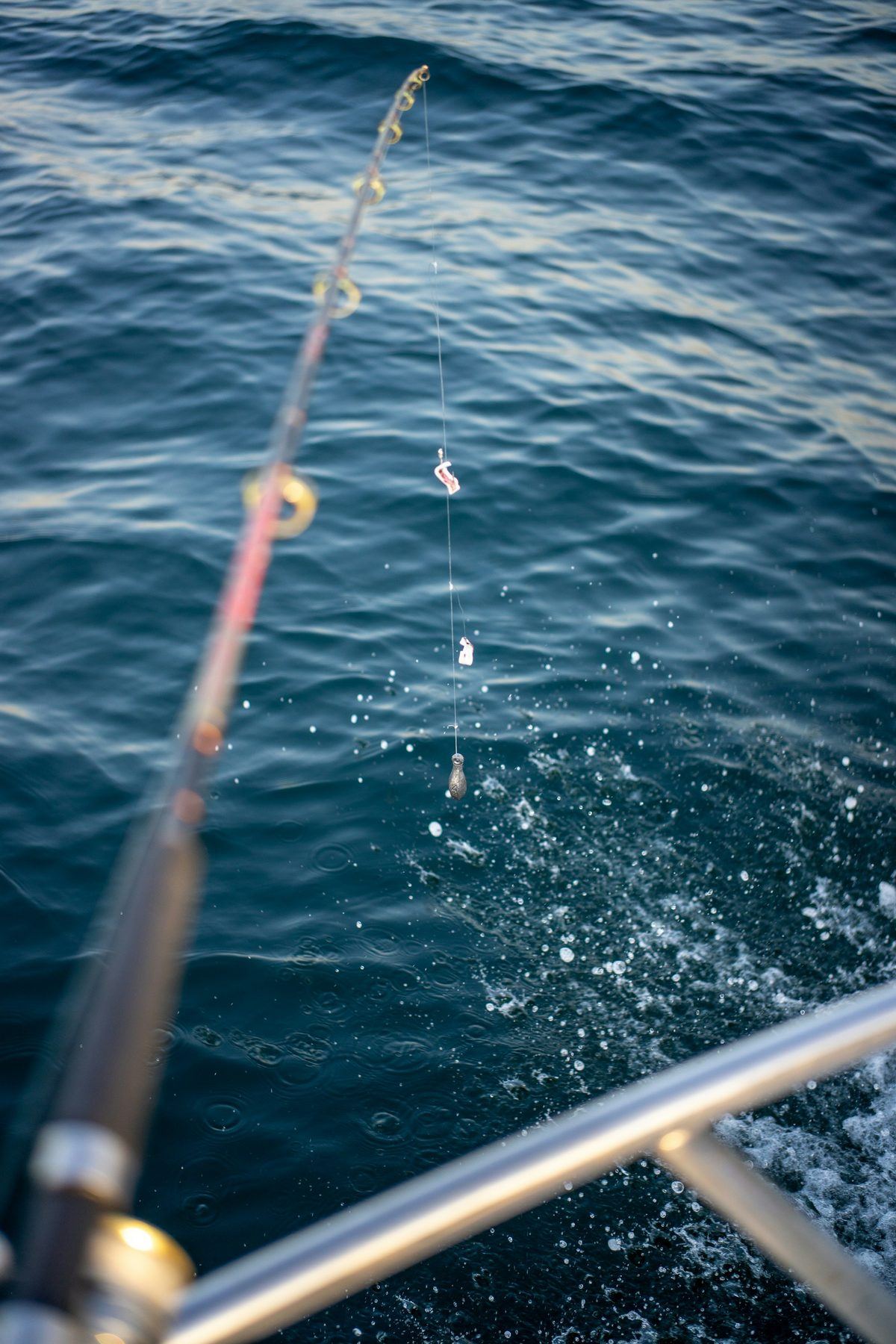 A fishing rod bent over deep blue open-ocean water beside a boat rail