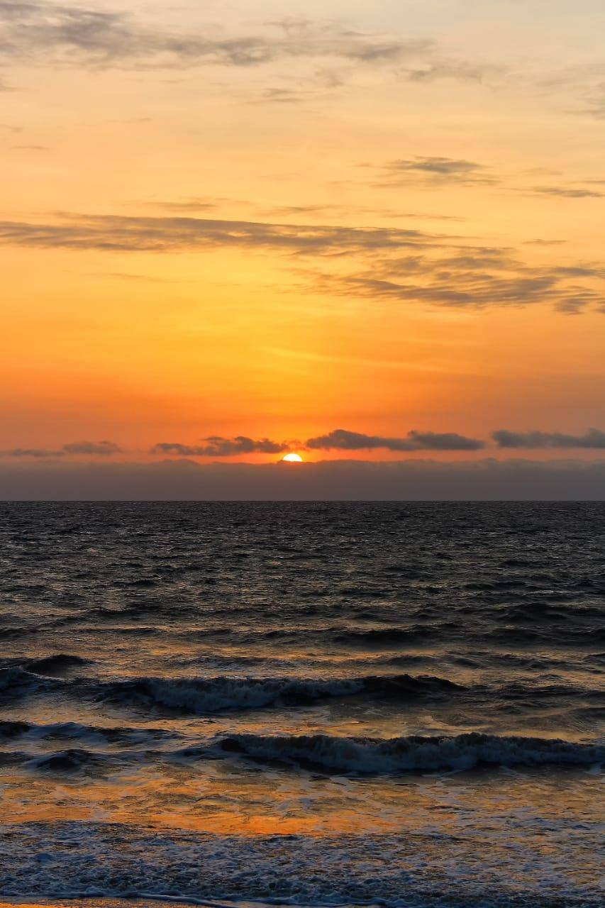 An orange Pacific sunset over rolling surf at El Tunco
